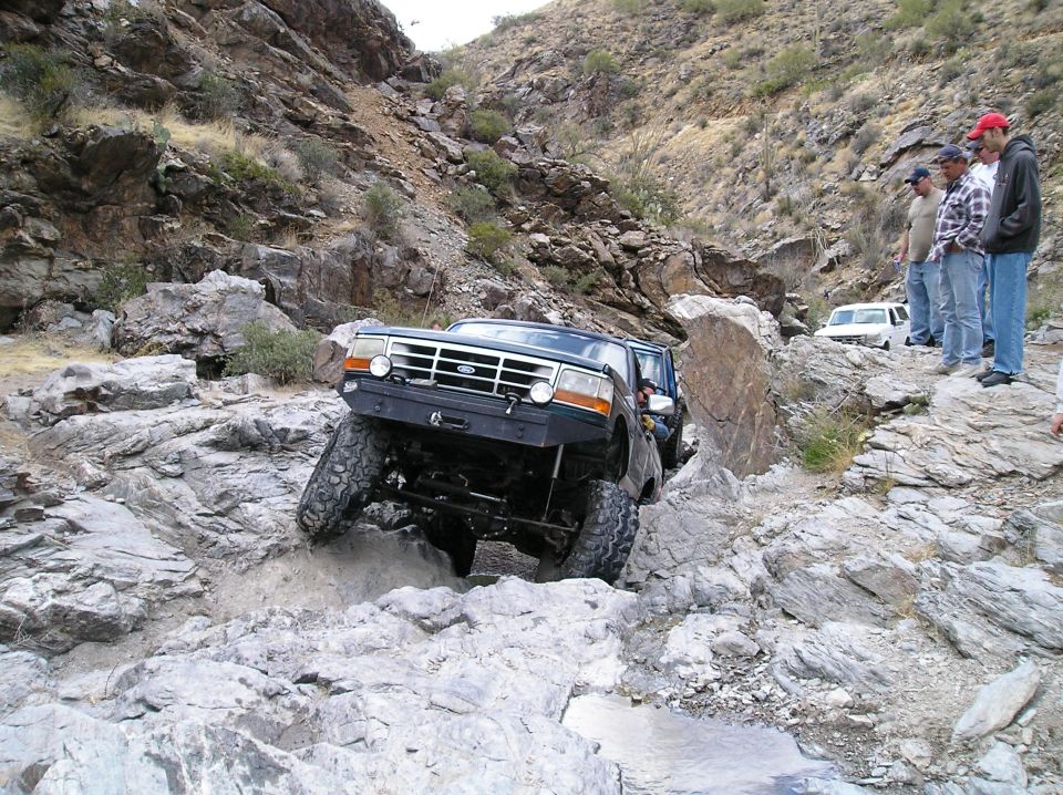 1993 Ford Bronco navigating a steep, rocky trail with a second vehicle visible in the background