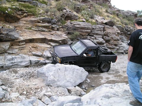 1993 Ford Bronco - Off-road pickup truck navigating difficult rocky terrain with a person watching.