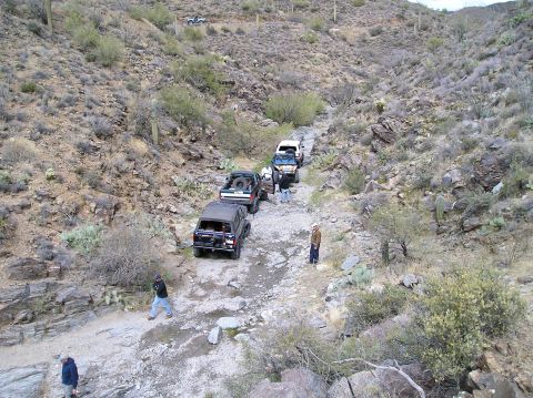1993 Ford Bronco - Several off-road vehicles navigate a , rocky path through a desert landscape.