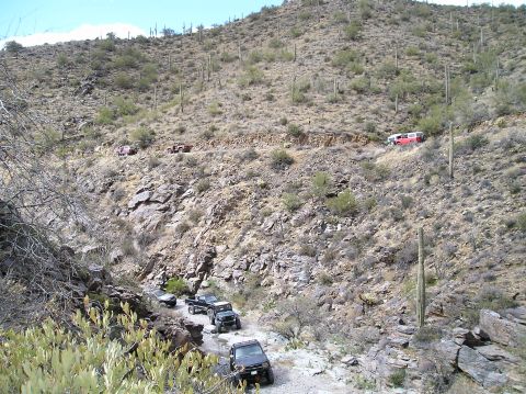 1993 Ford Bronco - Several off-road vehicles navigate a path winding up a desert hillside dotted with saguaro cacti.