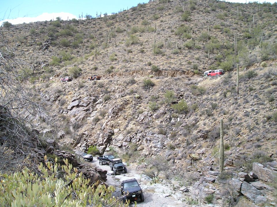Multiple SUVs and a van driving on a rocky desert trail