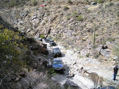 1993 Ford Bronco - A convoy of off-road vehicles navigates a challenging rocky trail in a desert landscape.