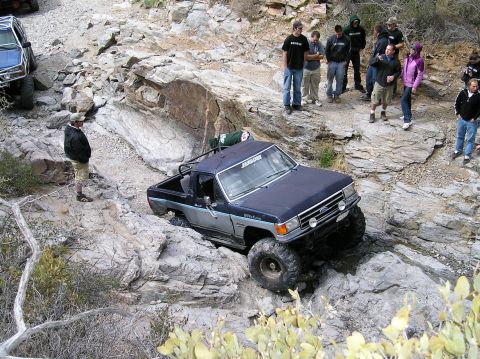 1993 Ford Bronco - A group of people watch as a modified pickup truck navigates a difficult rocky trail.
