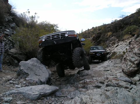 1993 Ford Bronco - Two off-road vehicles navigate a rocky trail with steep inclines and sparse vegetation.