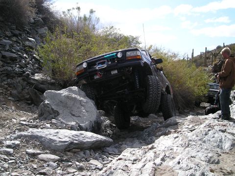 1993 Ford Bronco - A dark blue Ford Bronco navigates a rocky trail with a person watching.