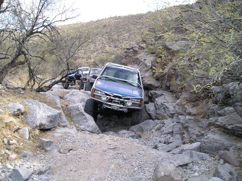 1993 Ford Bronco - Multiple off-road vehicles tackle a challenging rocky trail in a desert landscape.