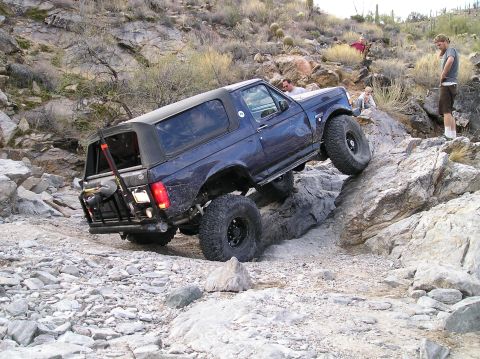 1993 Ford Bronco - A blue 1993 Ford Bronco navigates a challenging rocky trail, demonstrating its off-road capabilities.
