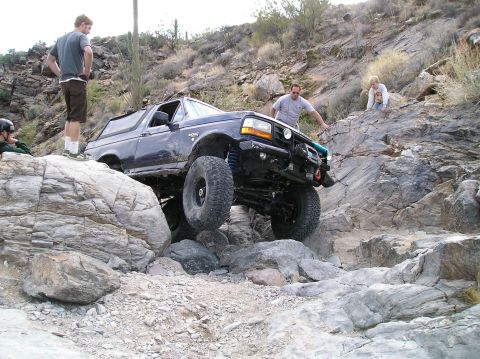 1993 Ford Bronco - A Ford Bronco is shown off-roading on a rocky trail with several people observing the action.