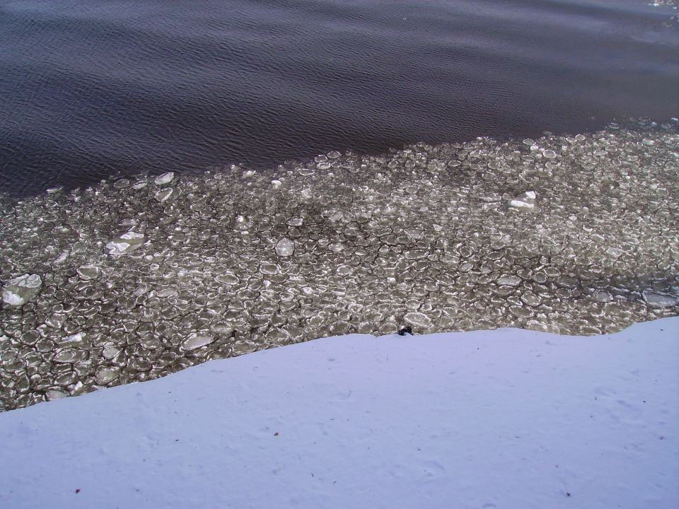 Ice floes on dark water with a snowy bank in the foreground. Supermotors.net logo in lower right