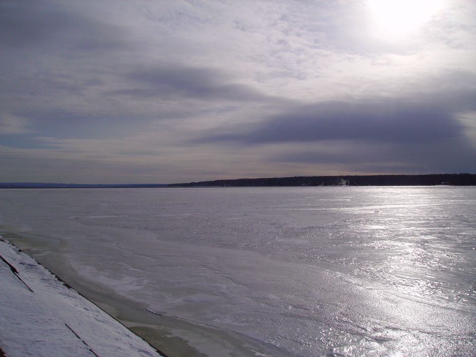 Frozen lake or river under a cloudy sky with sun glare