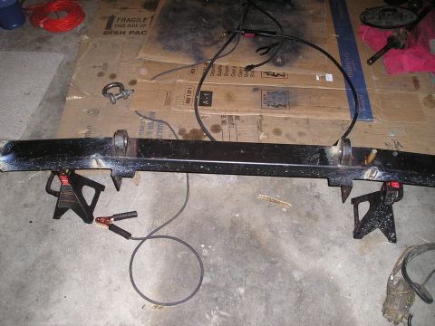 1986 Ford Bronco II - A black bumper, likely for a truck or SUV, is supported by jack stands and connected to welding equipment.