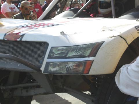 Close-up of white off-road race vehicle front headlights and fender with man filming