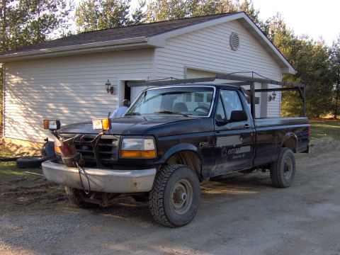 1995 Ford F-250 - This 1995 Ford F-250 pickup truck is equipped with a plow mount and a rack system, seen parked in front of a residential garage.