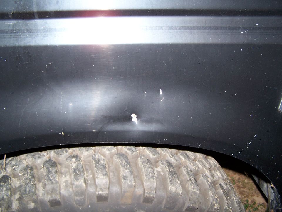 Dark vehicle fender panel above mud-terrain tire at night, with flash glare and scuffs