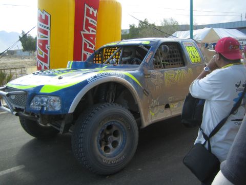 Mud-covered blue and green off-road race truck number 829 with BFGoodrich beside Tecate arch