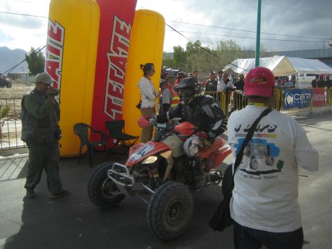 Rider on red Honda quad ATV near Tecate inflatable arch with marshals and crowd