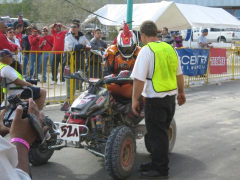 Rider on red and white quad ATV number 52A at start with marshal in yellow vest