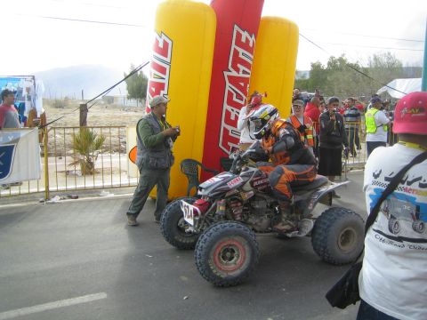 Rider on red quad ATV number 57A at street start near Tecate arch with marshals