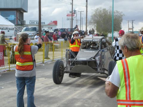 Off-road race buggy number 1217 at street start with marshals in safety vests directing