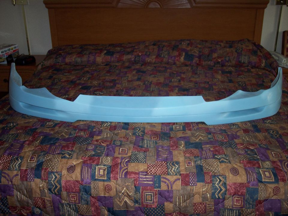 Light blue unpainted front lip spoiler body kit piece resting on a patterned bedspread
