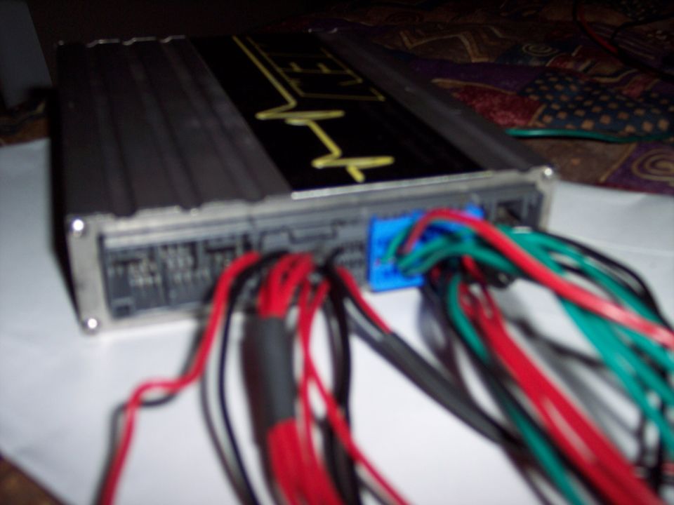 Black car amplifier with yellow graphic and many red, green, and black wires connected via a blue plug
