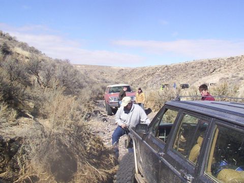 1978 Ford Bronco - Several off-road vehicles are seen on a challenging dirt trail in a dry, hilly landscape.