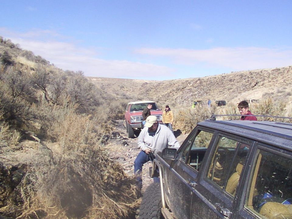 1978 Ford Bronco and other off-road vehicles navigating a rocky trail with brush on the sides