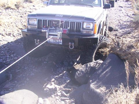 1978 Ford Bronco - A Jeep Cherokee XJ navigates a rocky off-road path, with a winch attached to its front bumper.