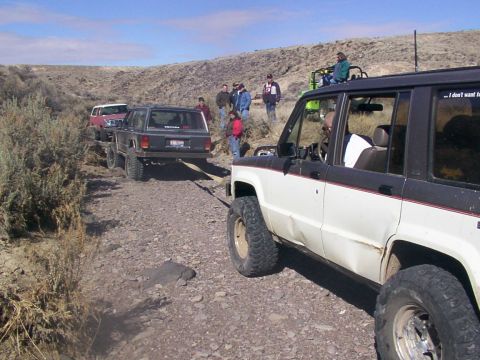 1978 Ford Bronco - Several off-road vehicles navigate a rough dirt track in a desert landscape.