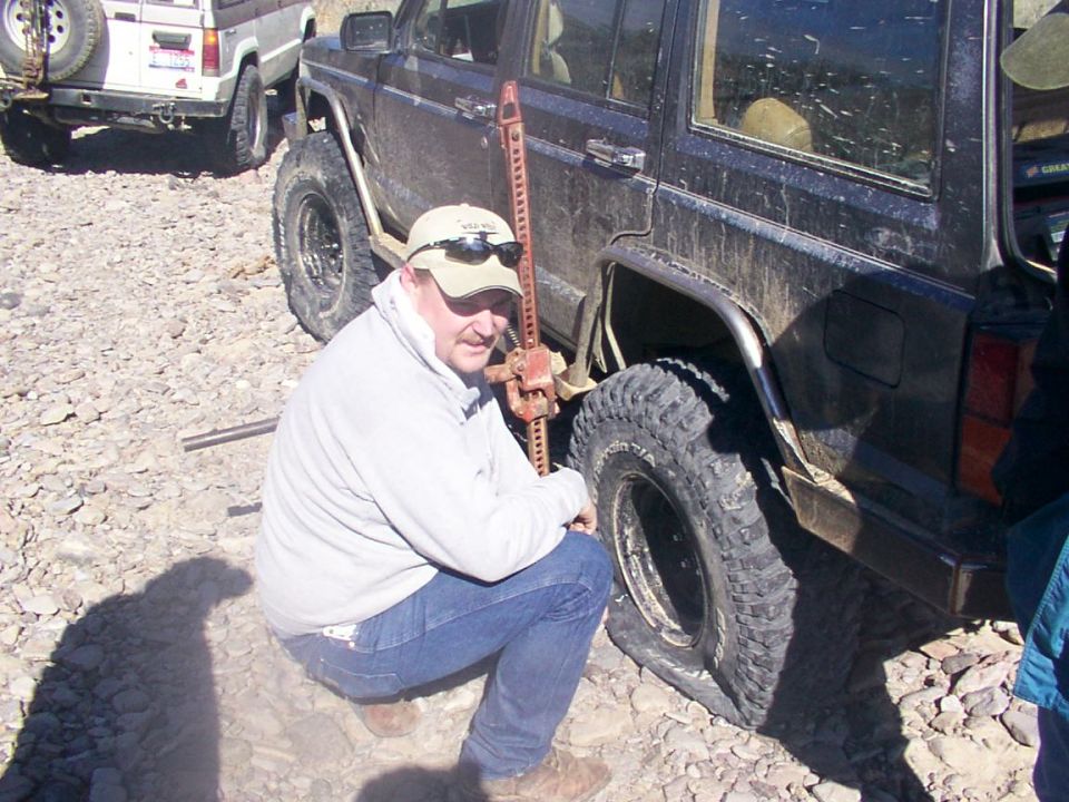 Man changing flat tire on dark off-road SUV with hi-lift jack
