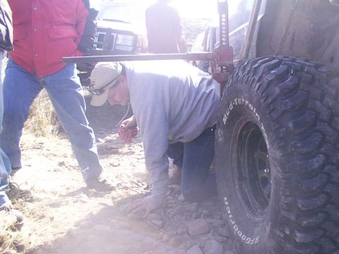 1978 Ford Bronco - People are working on a vehicle stuck in rough terrain, with a jack lifting a large tire.