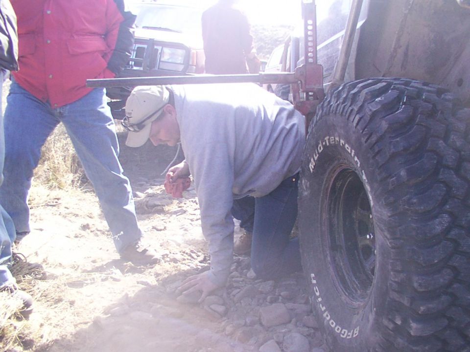 Guy jacking up a large tire on an off-road vehicle, another vehicle visible behind