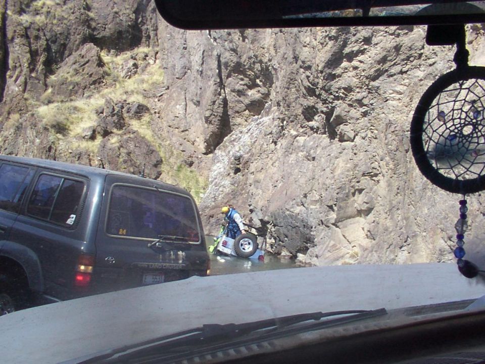 Dark SUV side view on rocky road; person near partially submerged vehicle in river