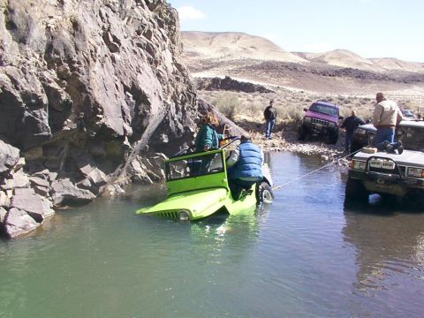 1978 Ford Bronco - Several vehicles are stuck in a shallow riverbed, with one green Jeep partially submerged.