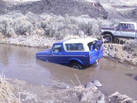 1978 Ford Bronco - Blue 1978 Ford Bronco partially submerged in a creek, with a second truck on the bank.