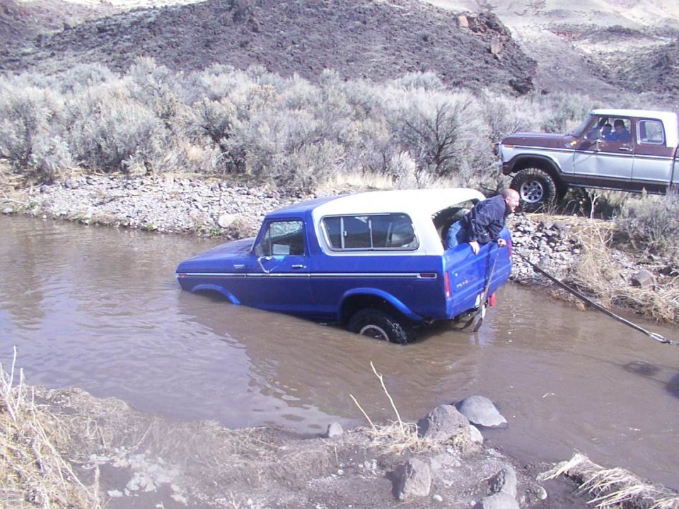 1978 Ford Bronco stuck in shallow water, another truck on bank