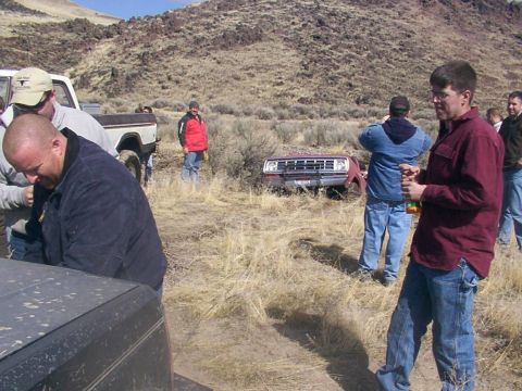 1978 Ford Bronco - A group of people stand around a red truck that appears to be stuck in a dry, hilly landscape.
