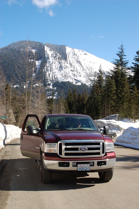 2006 Ford F-250 - A maroon Ford F-250 truck is parked on a dirt road with snow banks and a mountain in the background.