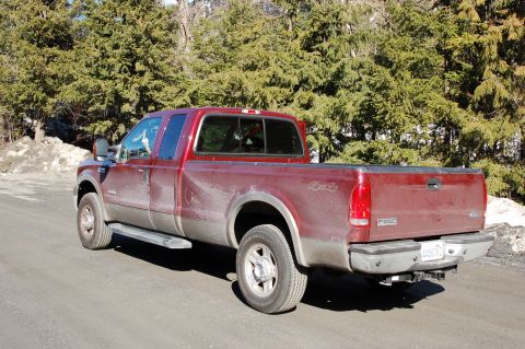 2006 Ford F-250 - This 2006 Ford F-250 pickup truck is seen from the rear three-quarter angle on a dirt road with trees in the background.