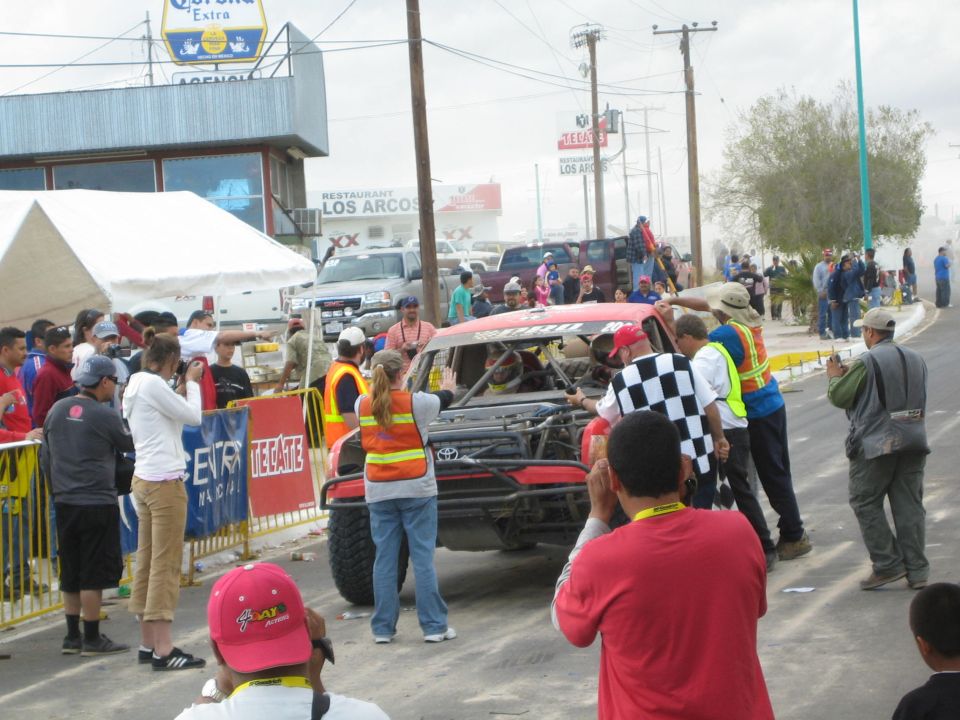 Crowd surrounding a race truck with a checkered flag on a town street