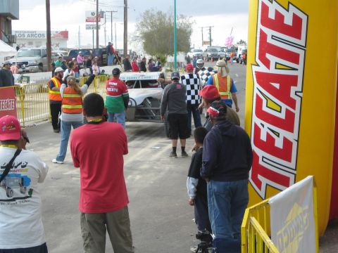 Spectators line a street beside a large yellow Tecate inflatable column at a race