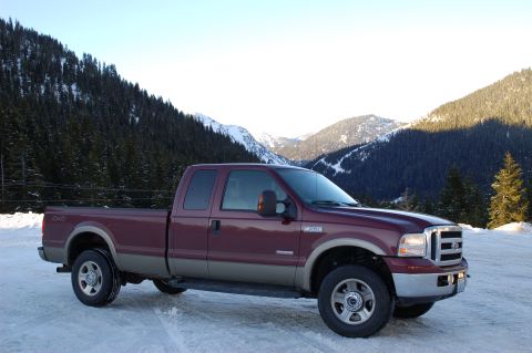2006 Ford F-250 - A maroon Ford Super Duty pickup truck is parked on a snowy road with mountains and pine trees in the background.
