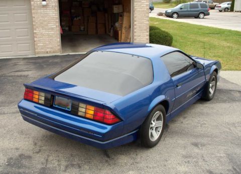 1990 Chevrolet Camaro - A blue Chevrolet Camaro is parked in front of a garage with boxes stacked inside.