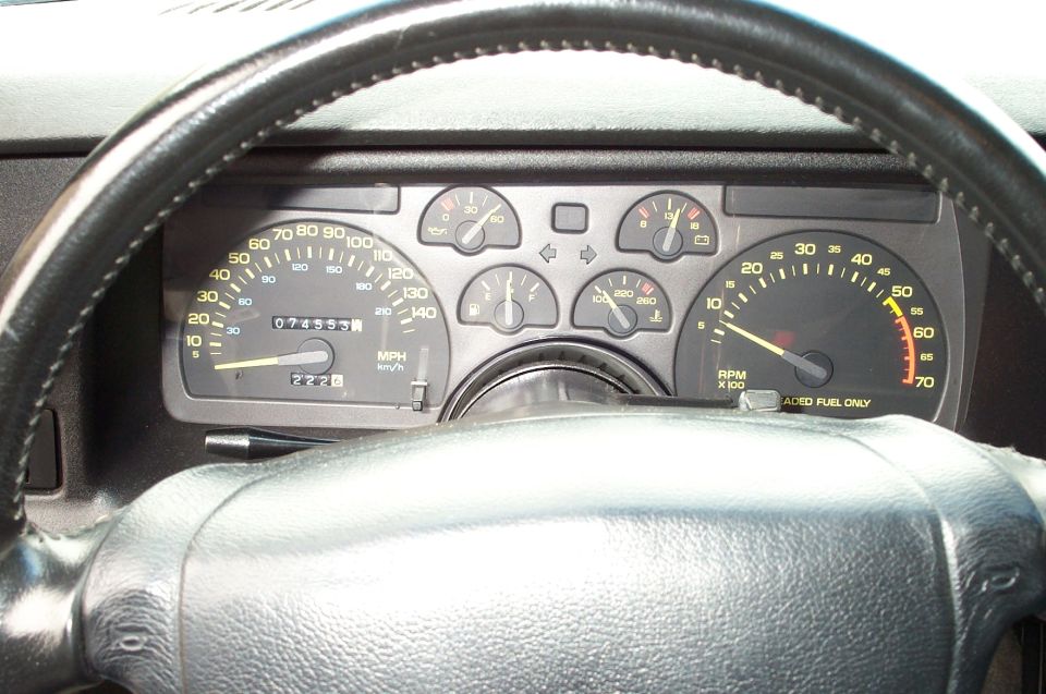 Car dashboard with speedometer, tachometer, and other gauges. Odometer reads 074555. Steering wheel is black