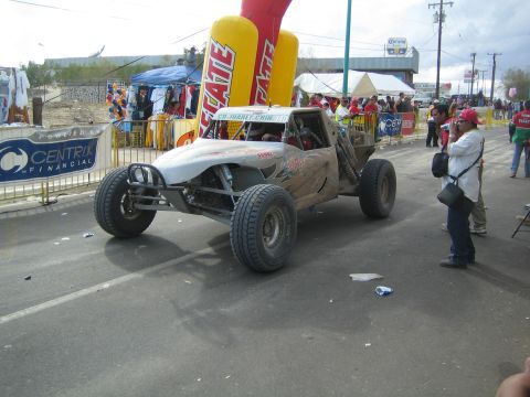 Silver open-cockpit tube-frame off-road buggy on a town street at a race