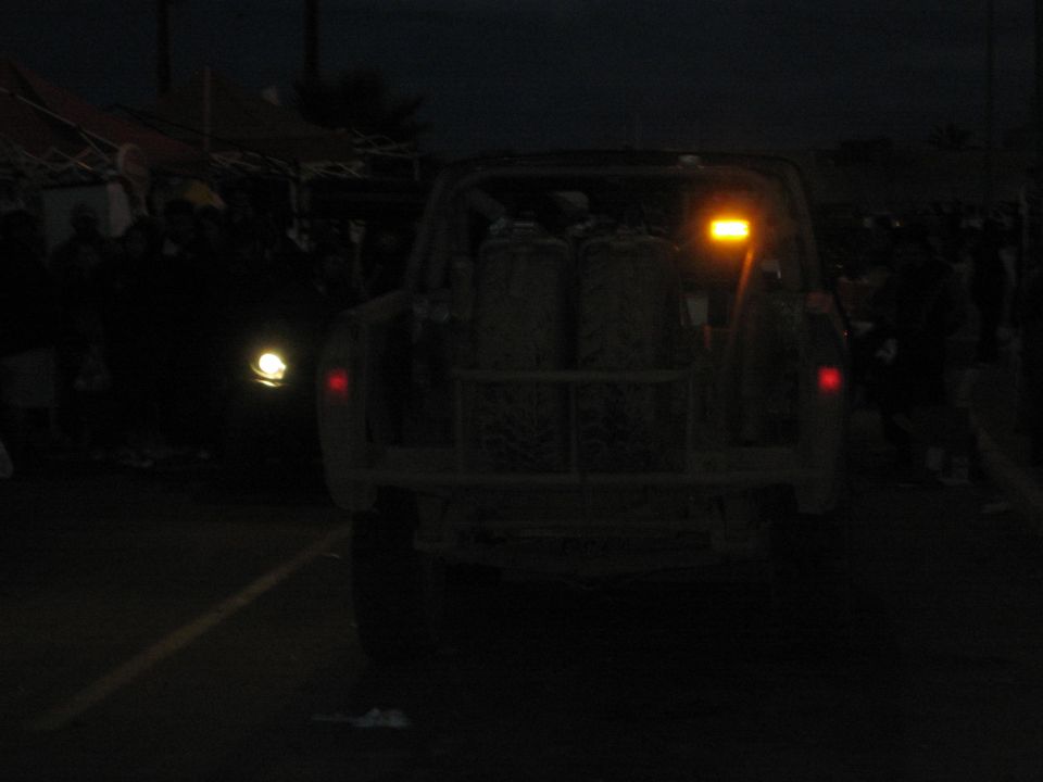Rear of an off-road truck at dusk with amber light and red taillights in a crowd
