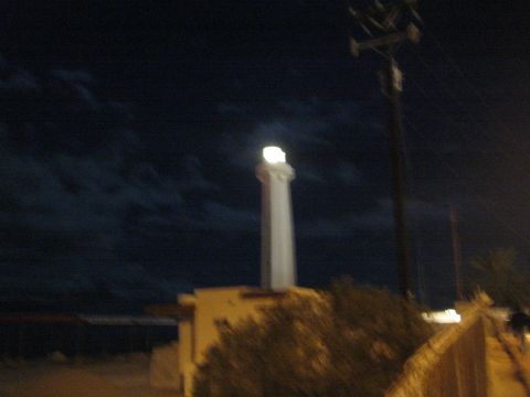 Blurry illuminated white lighthouse and power pole against a dark night sky