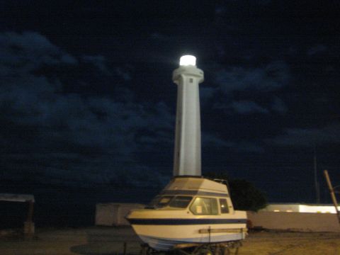 Lit white lighthouse mounted above a white and blue cabin boat at night