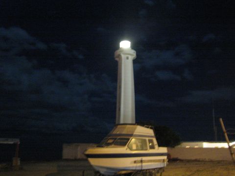 Lit lighthouse towering over a beached cabin cruiser boat at night