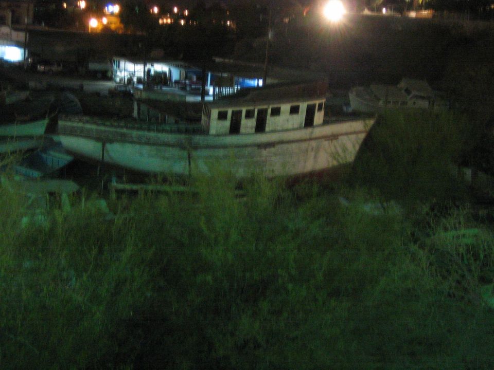Weathered wooden boat beached in tall grass with town lights at night